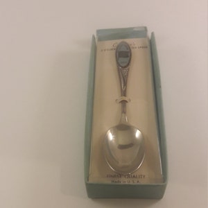 May include: A silver teaspoon with a blue and white enamel design of a clock tower. The spoon is in a white box with a green border. The box says "Finest Quality Made in U.S.A."