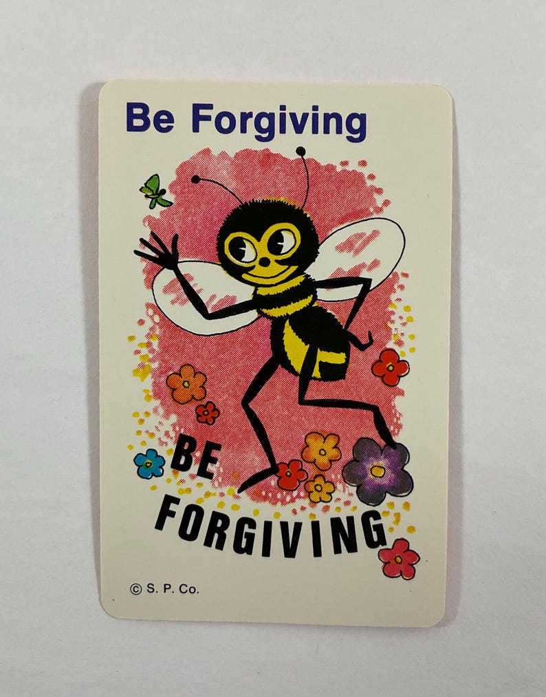Op de afbeelding: Een vintage kaart met de woorden "Be Forgiving" bovenaan en onderaan. In het midden staat een cartoonbij met een geel en zwart gestreept lichaam en grote ogen. Er zijn ook kleurrijke bloemen en een vlinder aanwezig.
