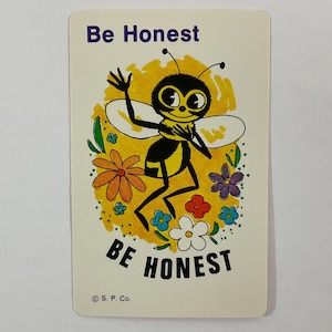 Op de afbeelding: Vintage kaart met een cartoon bijen illustratie. De bij, met een gele en zwarte body, zwaait. De kaart leest "Be Honest" in paars en "BE HONEST" in zwart. De bij is omringd door kleurrijke bloemen.