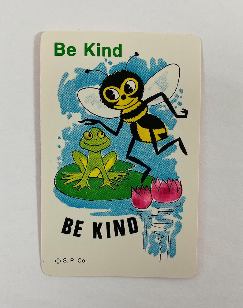 Op de afbeelding: Een vintage kaart met een cartoon illustratie van een bij en een kikker. De bij is zwart en geel, en de kikker is groen. De kaart heeft de woorden "Be Kind" in groene en zwarte tekst.