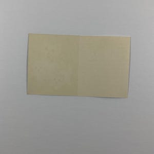 K&ouml;nnte beinhalten: Eine rechteckige, cremewei&szlig;e Klappkarte in flach ge&ouml;ffneter Position. Die Papieroberfl&auml;che wirkt glatt und matt und weist auf der linken Seite ein dezentes, helles, sich wiederholendes florales Muster auf.