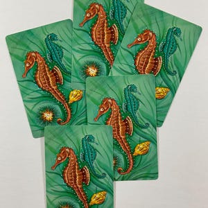 May include: Five rectangular cards featuring a green underwater scene with flowing seaweed. Each card displays a large brown seahorse, a smaller teal seahorse, a spiky orange sea urchin, and a yellow seashell, all rendered in a detailed illustration.