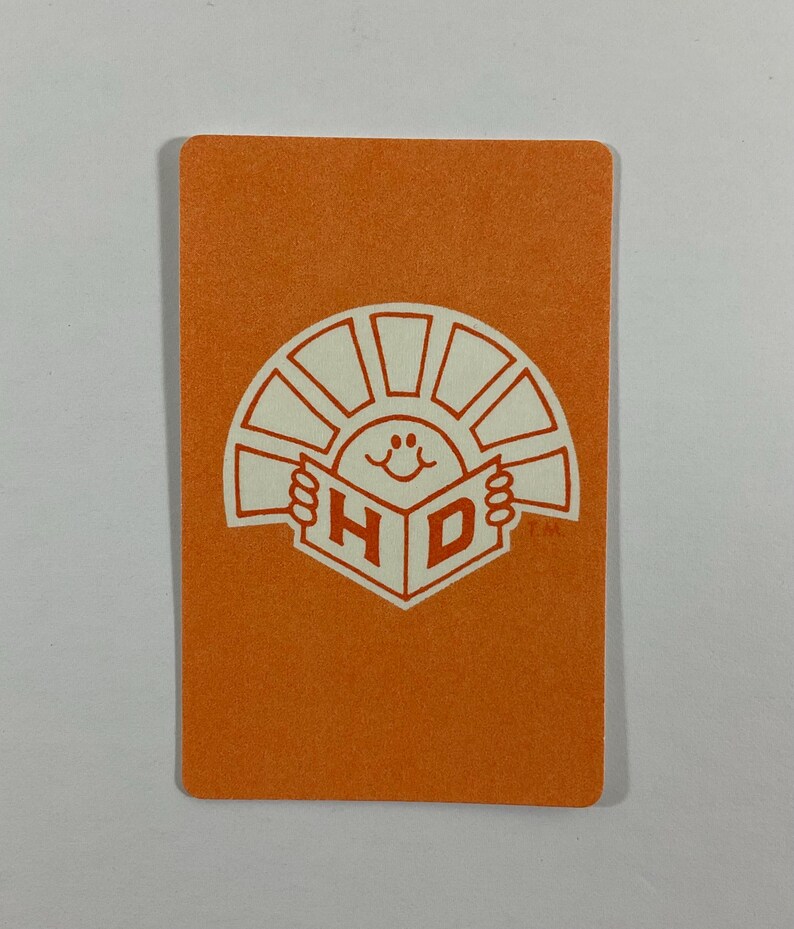 Op de afbeelding: Oranje rechthoekige kaart met een wit logo met een lachende zon die een boek vasthoudt met de letters "H" en "D". De kaart heeft afgeronde hoeken en een getextureerd oppervlak.
