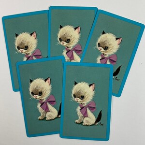 May include: Six playing cards with a blue border and a light blue background. Each card features a cartoon illustration of a white kitten with a pink bow. The kittens are all facing the right side of the card. The text "Chm" is printed in the bottom right corner of each card.