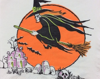 May include: A Halloween-themed napkin featuring a witch flying on a broomstick against an orange circle. The witch is wearing a black hat and cloak. The design includes a haunted house, bats, tombstones, and a skull.