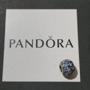 May include: A silver charm with blue and clear crystals, featuring the word "PANDORA" on a white background.
