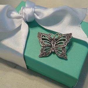 May include: A silver butterfly brooch with a marquetry design, set in a turquoise gift box with a white satin ribbon.