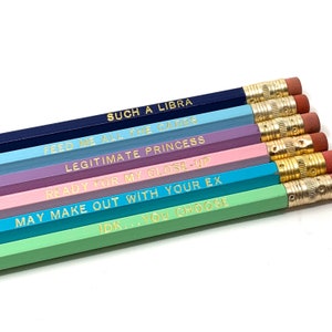 May include: Set of six wooden pencils with different colored paint and gold lettering. The pencils have the following phrases printed on them: "Such a Libra", "Feed me all the carbs", "Legitimate Princess", "Ready for my close-up", "May make out with your ex", and "IDK... you choose".