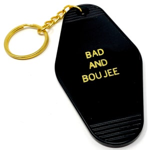 May include: Black motel key chain with a gold chain and the text "BAD AND BOUJEE" in gold lettering.
