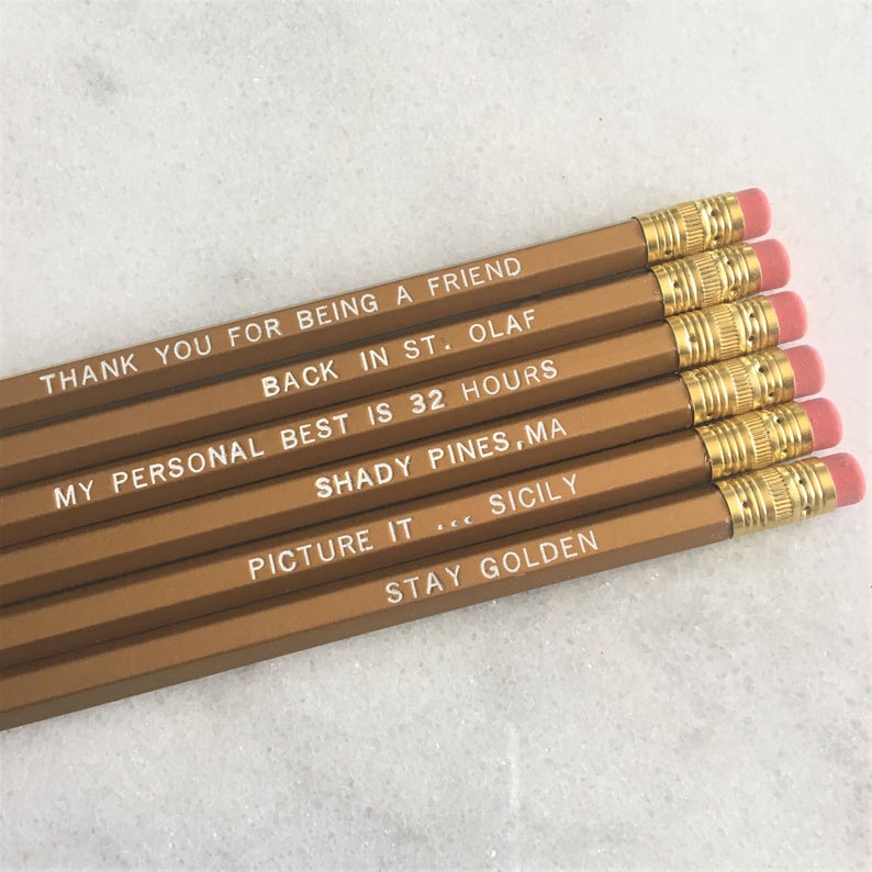 May include: Six gold pencils with white text. The text on the pencils reads: "Thank you for being a friend", "Back in St. Olaf", "My personal best is 32 hours", "Shady Pines, MA", "Picture it... Sicily", and "Stay Golden".