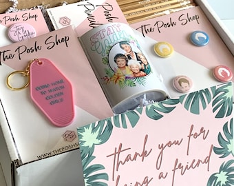 Peut inclure: Une boîte cadeau rose remplie de cadeaux sur le thème des Golden Girls, dont une tasse, un porte-clés et une carte qui dit "Merci d'être un(e) ami(e)".