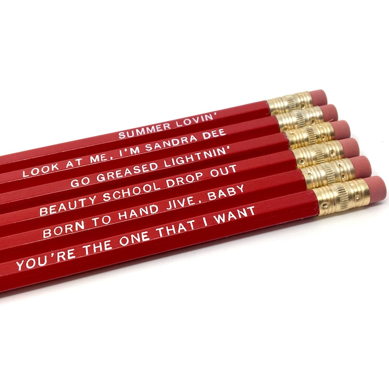 May include: Set of six red pencils with white text. The pencils feature lyrics from the musical Grease. The text on the pencils reads: "Summer Lovin', Look at me, I'm Sandra Dee, Go Greased Lightnin', Beauty School Drop Out, Born to Hand Jive, Baby, You're the One That I Want."