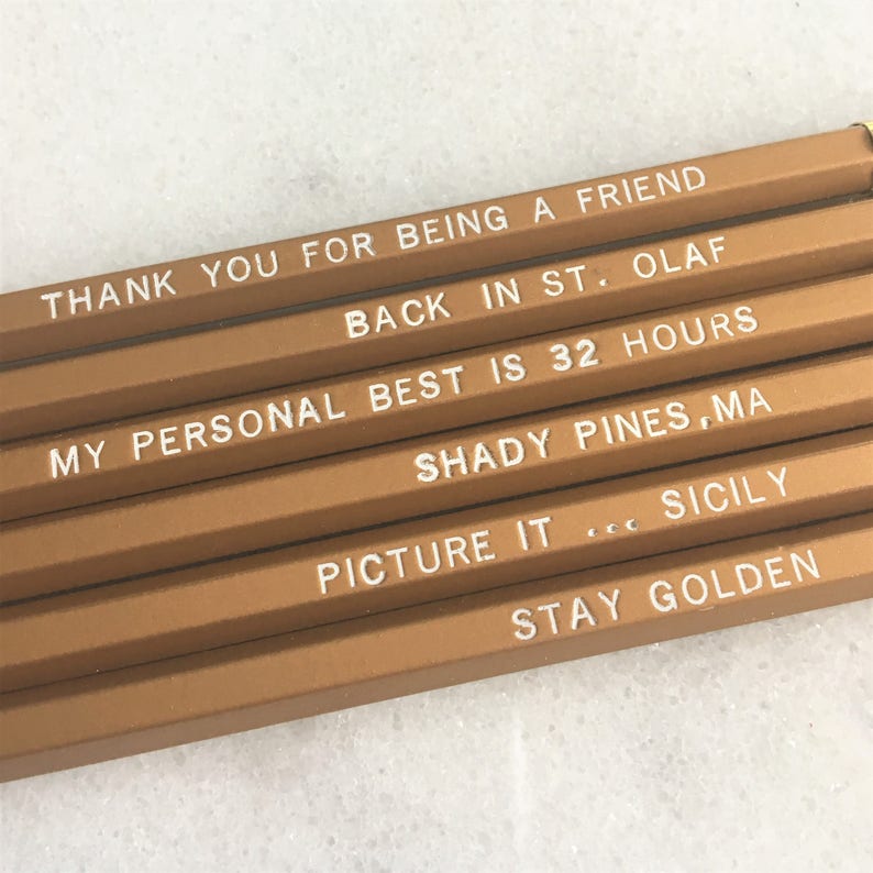 May include: Set of six gold pencils with white text. The text on the pencils reads: "Thank you for being a friend", "Back in St. Olaf", "My personal best is 32 hours", "Shady Pines, MA", "Picture it... Sicily", and "Stay Golden".