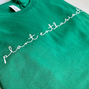 May include: A green t-shirt with the text "plant enthusiast" written in white cursive.