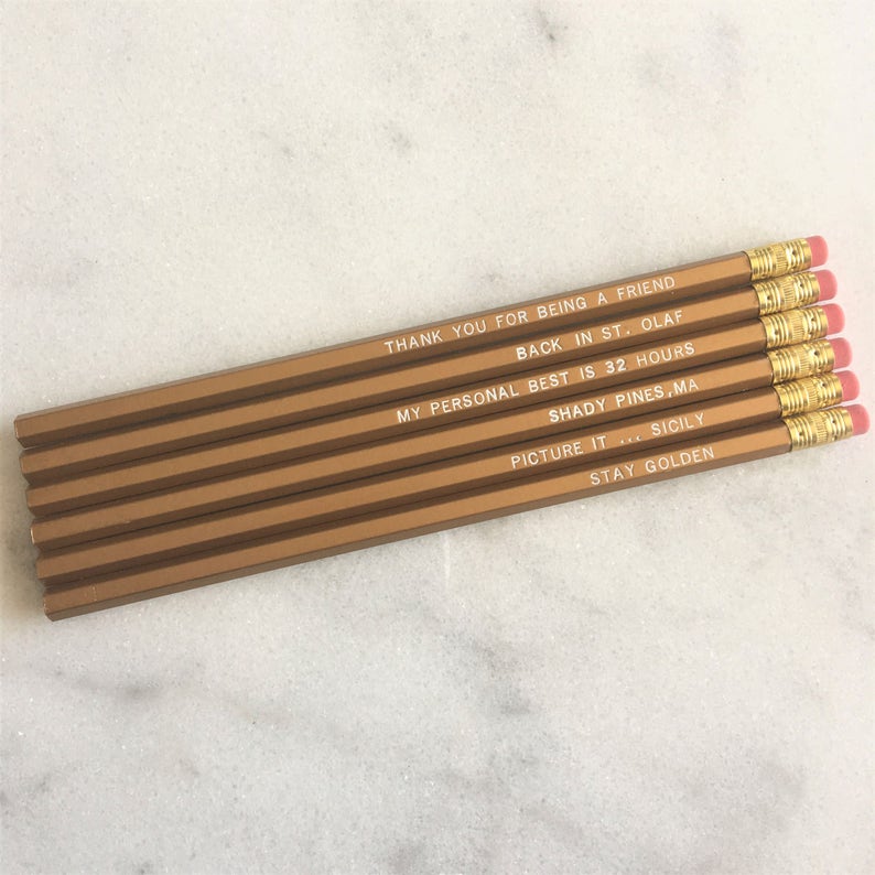 May include: Set of six gold pencils with white text. The text on the pencils reads: "Thank you for being a friend", "Back in St. Olaf", "My personal best is 32 hours", "Shady Pines, MA", "Picture it... Sicily", and "Stay Golden".