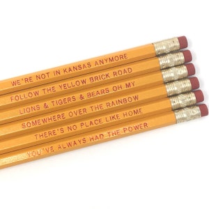 May include: Six yellow pencils with red text printed on them. The text on the pencils reads: "We're not in Kansas anymore", "Follow the yellow brick road", "Lions & tigers & bears oh my", "Somewhere over the rainbow", "There's no place like home", and "You've always had the power".