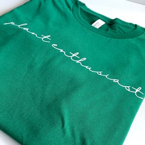 May include: A green t-shirt with the text "plant enthusiast" written in white cursive.