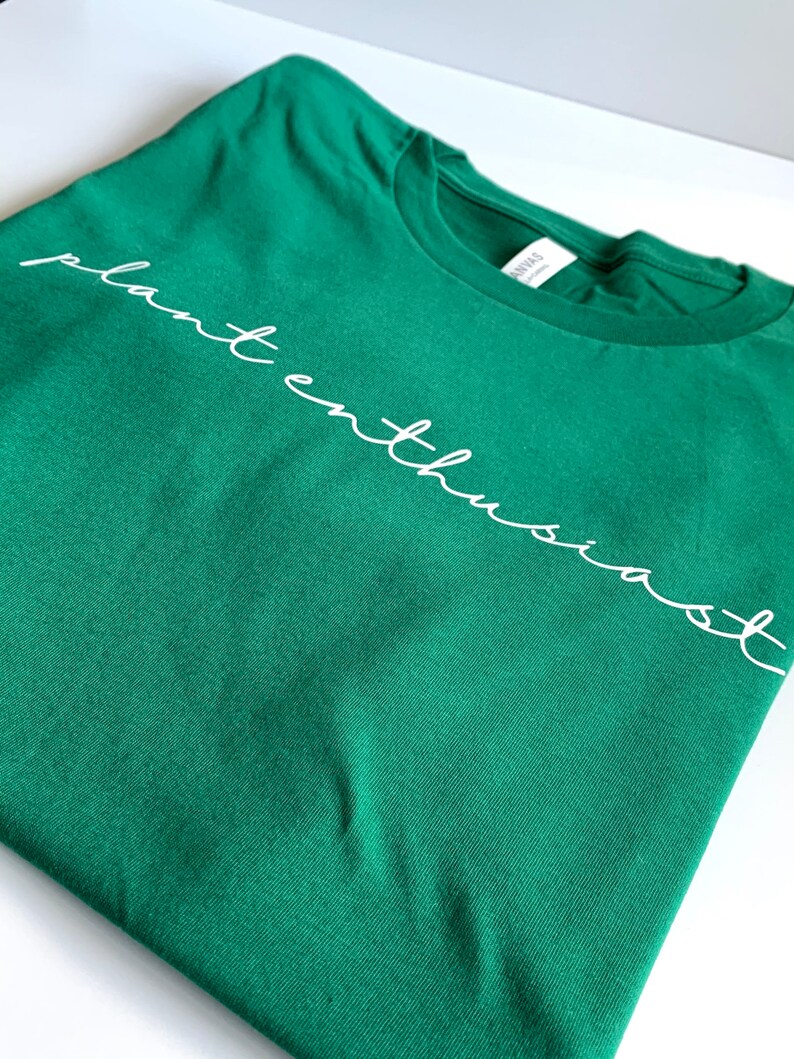 May include: A green t-shirt with the text "plant enthusiast" written in white cursive.