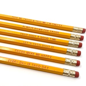 May include: Six yellow pencils with red text. The pencils have different taco-themed sayings, including "Feed me tacos & tell me I'm pretty", "Always down for tacos", "Taco bout a good time", "Let's taco bout it", "Tacos make me happy", and "Every day is taco day".