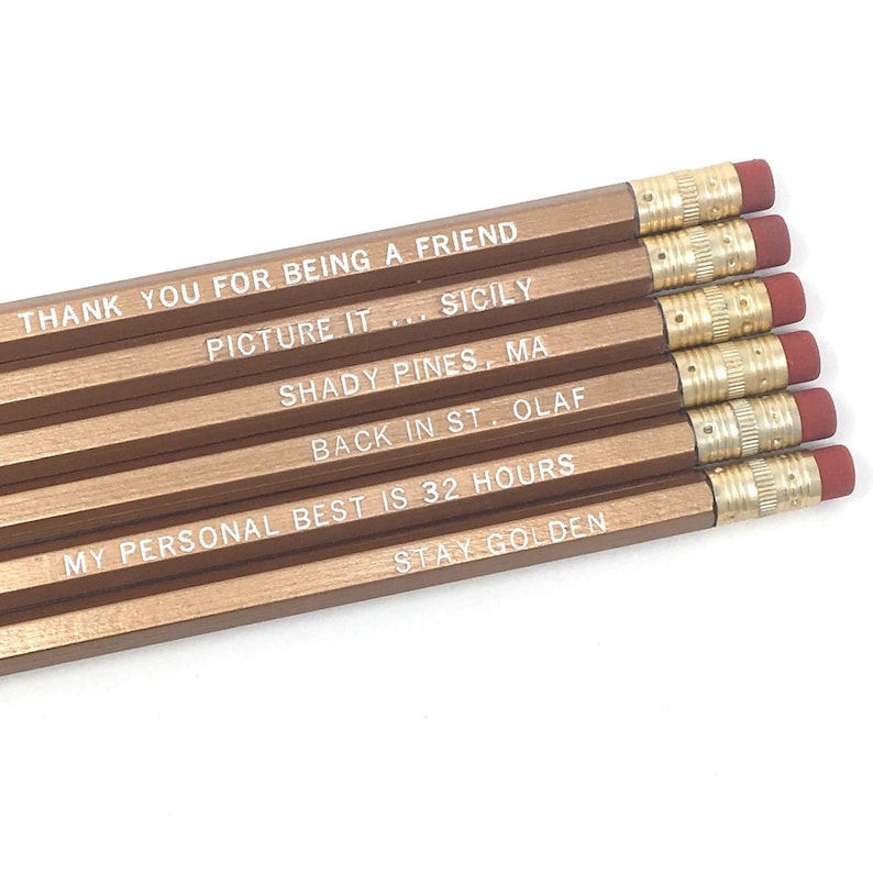 May include: Six gold pencils with white text on each. The text reads: "Thank you for being a friend", "Picture it... Sicily", "Shady Pines, MA", "Back in St. Olaf", "My personal best is 32 hours", and "Stay Golden".