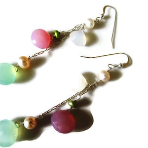 Może przedstawiać: Para kolczyków wiszących ze srebrnym łańcuszkiem i pastelowymi kamieniami. Kolczyki mają jasnoniebieskie, różowe i białe kamienie, a także małe zielone koraliki.