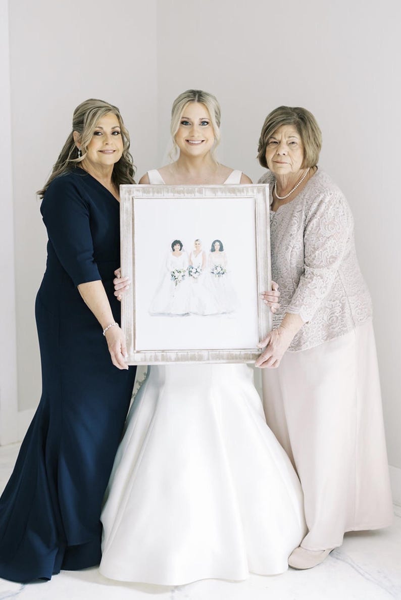 K&ouml;nnte beinhalten: Drei Frauen halten ein gerahmtes Aquarellportr&auml;t von drei Frauen in Brautkleidern. Die Frauen tragen formelle Kleider in Marineblau, Wei&szlig; und Beige. Das Portr&auml;t hat einen wei&szlig;en Rahmen.