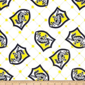 May include: White fabric with a repeating pattern of yellow and black Hogwarts house crests. Each crest features a badger, the words "Hufflepuff" and a star. The background is a white and yellow diamond pattern.
