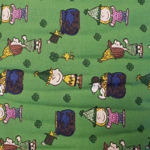 May include: Green fabric with a repeating pattern of cartoon characters wearing green hats and holding pots of gold. The characters are surrounded by four-leaf clovers.