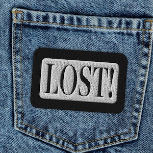 May include: A pair of blue denim jeans with a black patch on the back pocket that says "LOST!" in white lettering.