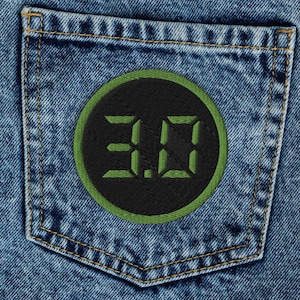 Puede incluir: Vaqueros de mezclilla azul con lavado ácido, diseño de cintura alta y un bolsillo trasero. Un parche circular negro está cosido en el bolsillo, mostrando el texto digital verde 3.0 con un borde verde a juego alrededor del parche.