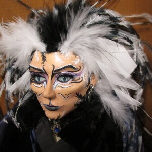 May include: A doll with black and white feathers in its hair. The doll has white face paint with black and purple accents. The doll is wearing a black and white outfit.