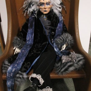 May include: A doll with white hair and a black and blue outfit sits on a wooden chair. The doll has a painted face with blue eyeshadow and a black and white fur collar.