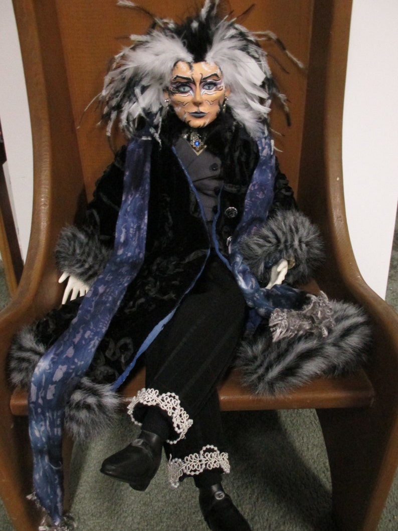 May include: A doll with white hair and a black and blue outfit sits on a wooden chair. The doll has a painted face with blue eyeshadow and a black and white fur collar.