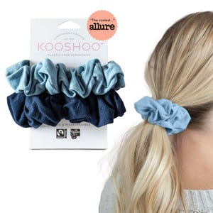 Puede incluir: Un conjunto de tres scrunchies azules y azul marino hechos de tela libre de plástico. Los scrunchies están empaquetados en una caja blanca con el nombre de la marca "KOOSHOO" y el texto "Scrunchies libres de plástico". La caja también tiene un logotipo certificado Fairtrade y GOTS.