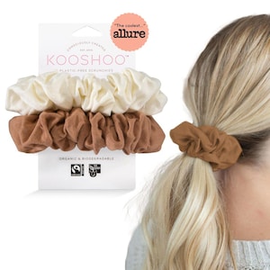May include: Three fabric scrunchies in a set. One is brown, one is white, and one is a combination of both. The scrunchies are made from organic and biodegradable materials. The packaging says "KOOSHOO" and "Plastic-Free Scrunchies".