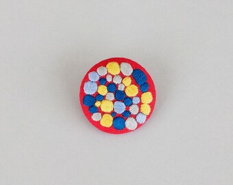 Brooch with embroidery style colored beads on red background