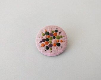 Brooch with embroidery style colored pearls on pink background