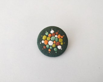Brooch with embroidery style colored pearls on dark green background