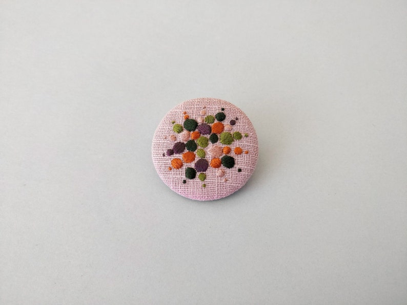 Brooch with embroidery style colored pearls on pink background image 1