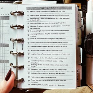 May include: A self-care list printed on a small notepad, held open with silver rings. The list includes activities like exercise, healthy eating, and meditation. The notepad is open to a page with the title "SELF-CARE LIST".