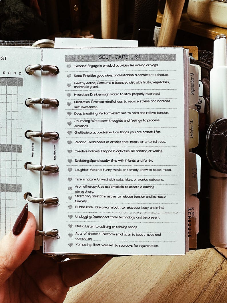 May include: A self-care list printed on a small notepad, held open with silver rings. The list includes activities like exercise, healthy eating, and meditation. The notepad is open to a page with the title "SELF-CARE LIST".