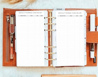 May include: A tan leather six-ring binder open to two pages titled DECLUTTERING CHECKLIST with columns for description, area, due, and done. The binder features a gold metal ring mechanism, two pens, and a tab labeled TODAY. Below are decorative tape rolls.