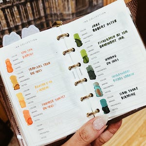 May include: A white ceramic mug with a black handle and the text "But First, Coffee" in a black, handwritten-style font. The mug is on a white surface.