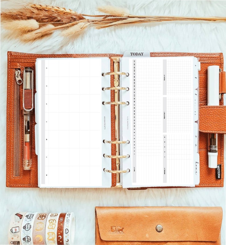 May include: A tan leather six-ring binder planner open to a grid-lined page with a 'TODAY' tab. The planner includes a clear pen loop with a fountain pen, a white pen, and a zippered pocket. Below are five rolls of patterned washi tape and a tan leather case.
