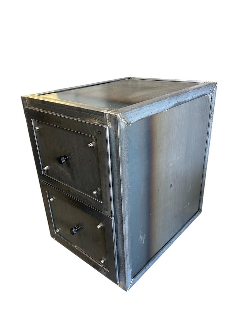 May include: A two-drawer metal cabinet with a welded frame. The cabinet has a dark, industrial finish with visible weld marks. Each drawer features a black knob and is secured with screws. The overall design is boxy and modern.