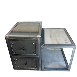 May include: A metal nightstand with two drawers and a side shelf. The nightstand has an industrial, raw finish. The drawers have black knobs. The side shelf features a light-coloured wooden surface.