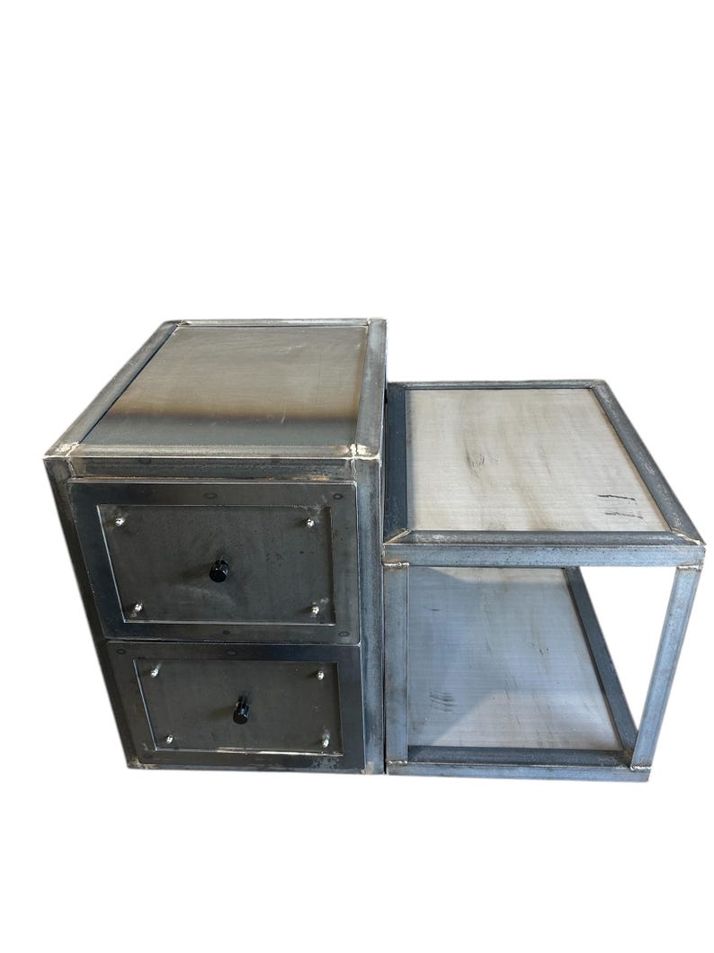 May include: A metal nightstand with two drawers and a side shelf. The nightstand has an industrial, raw finish. The drawers have black knobs. The side shelf features a light-coloured wooden surface.