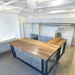 May include: A large, L-shaped desk with a walnut wood top and a black metal frame. The desk has a wire mesh panel underneath the top.