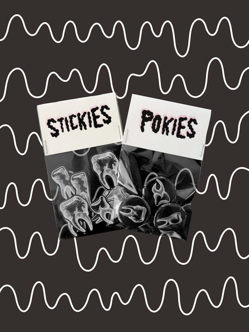 May include: Two clear plastic bags filled with enamel pins. One bag has a white label with the text "STICKIES" in black. The other bag has a white label with the text "POKIES" in black. The pins in the first bag are white tooth shapes. The pins in the second bag are black and feature a tooth shape.