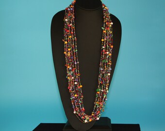 May include: Multi-strand necklace with colorful beads, including red, orange, yellow, green, blue, purple, and white beads. The necklace is displayed on a black mannequin.